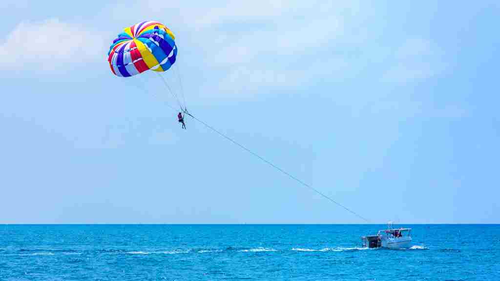 青い海に浮かぶボートから伸びるパラシュート。パラセーリングの画像