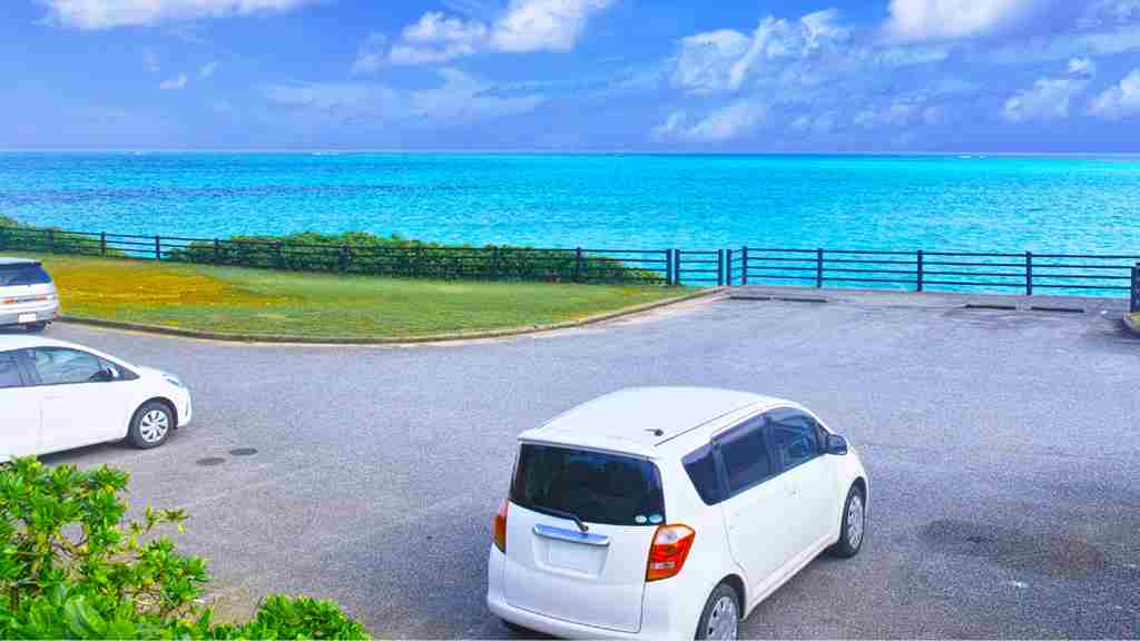 青い海が背景に海沿いの駐車場に白いミニバンが隙間を開けて2台止まっている画像