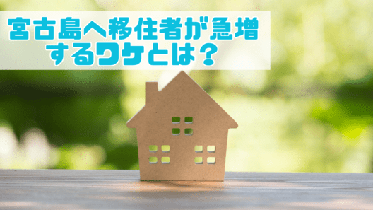 ぼやけた森林の背景の左上に”宮古島へ移住者が急増するワケとは？”と記載され茶色の家のミニチュアがテーブルに置かれている画像