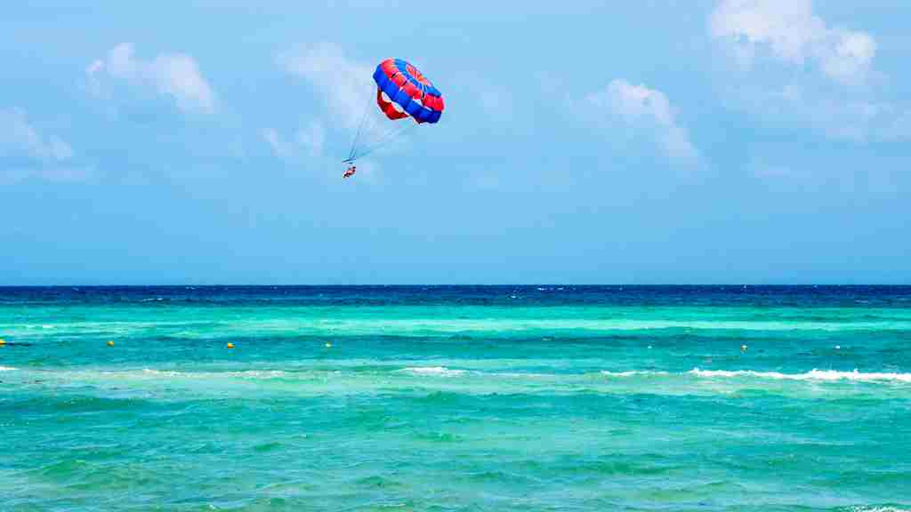 青い空にエメラルドグリーンの海。空には赤と青のパラセーリングのパラシュートが飛んでいる画像