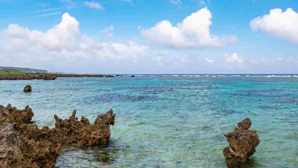 ゴツゴツとした岩々の海岸に水平線の見える青い海と青い空の画像