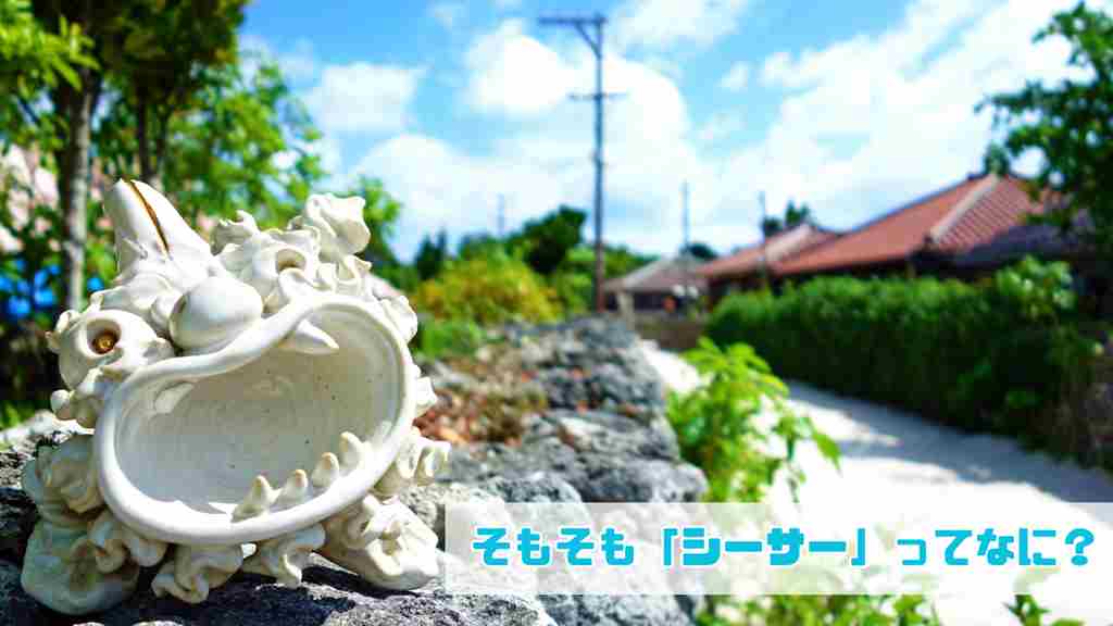 右下に”そもそも「シーサー」ってなに？”と記載。沖縄の住宅街と道路の背景に白く大きな口を開けたシーサーの置物が正面を向いている画像