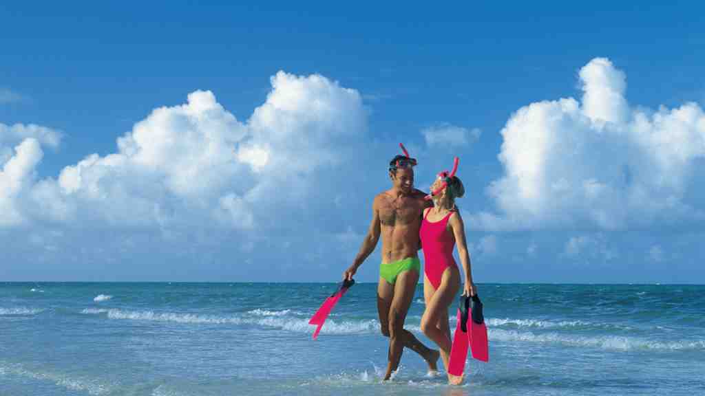 海と青空が広がる背景に水着姿の男女二人が肩を組み微笑んでいる画像